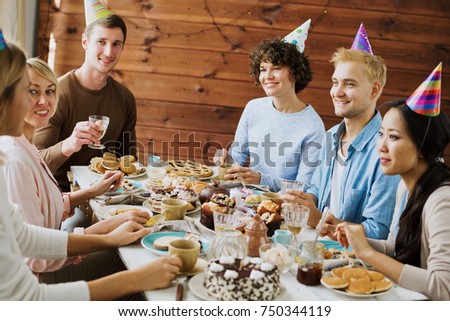 Cheerful friends having fun by birthday table during dessert with tea