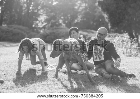 Black and white image of happy family of three playing in the park with their dog. Animal lovers. Mother, father, daughter and their dog