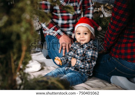 Christmas family portrait of young happy smiling parents playing with small kid in red santa hat near the christmas tree. Winter holiday Xmas and New Year concept.