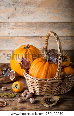 Two orange pumpkins and persimmons in basket with autumn dry leaves walnuts on wooden background butternut squash fall food vegetables concept selective focus with rustic style wooden table copy space