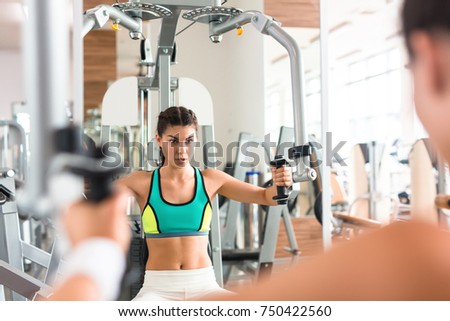 Slim young woman with dumbbells pumping muscles in front of mirror in gym