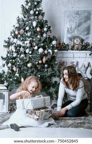 Mother and daughter open gifts under the Christmas tree. Woman and girl sitting under the tree and open presents. Christmas morning. A family.