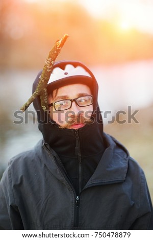 Artistic portrait of young pranksters of man with the big red mustache with glasses and a bike helmet and with a dry branch under the bonnet on blurred background of the Park. Close-up