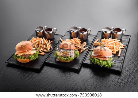 various burgers with french fries hamburgers on black plates. Buns with sesame seeds, sauces, on gray background