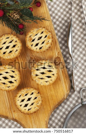 Fresh golden brown lattice top mince pies on a wooden bread board with a christmas motif