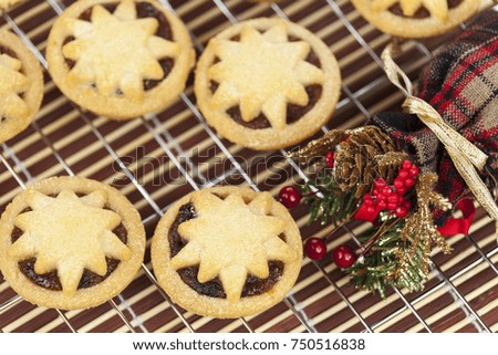 Freshly baked mini star topped mince pies on a cooling rack with a christmas acorn and berry arrangement