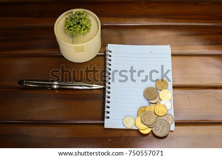 Creative layout made of coins, pen, note book and decoration isolated on wood background. Business, financial, job, saving and listing concept. Selective focus.