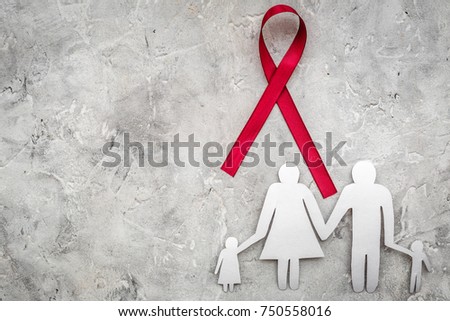 Red ribbon for HIV, AIDS, substance-abuse and anorexia awareness near paper silhouette of family on grey stone background top view copyspace