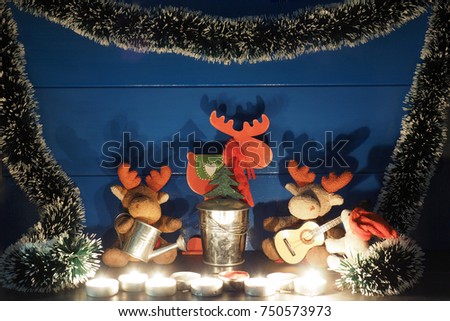 Two toy Christmas moose, or elks, sitting by a small Christmas tree near the blue wall with a candle, a guitar and romantic silhouettes in wooden rural house; medium shadows