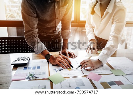 Young businessmen and partnership holding a pen pointing the graph to analyze the marketing plan with calculater and laptop computer on wood desk in office. Royalty-Free Stock Photo #750574717