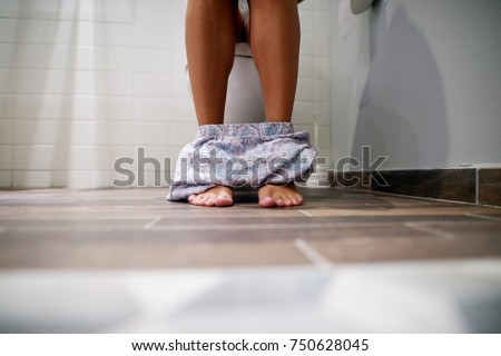 Close up of legs and panties of a woman sitting in a toilet room.