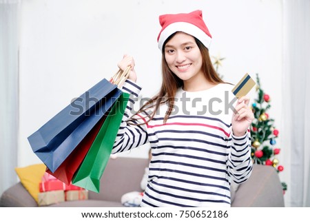 Young cute asian woman wearing Christmas hat smiling while holding shopping bags and credit card, Christmas shopping concept