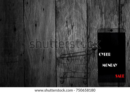 cyber monday sale text on mobile phone and shopping cart dark wooden background