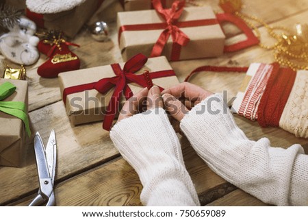 Christmas gift wrapping background. Female hands packaging christmas present with red ribbon, top view. Winter holidays concept, flat lay. Woman holding a Christmas gift to a red ribbon.