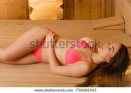 Portrait of young woman relaxing in wooden finnish sauna. Attractive girl in bikini resting. Spa wellbeing pleasure.