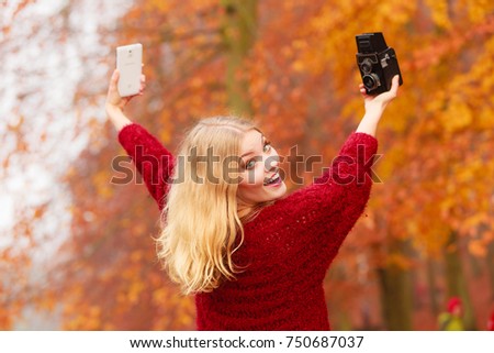 Pretty smiling woman in fall forest park taking selfie self photo with old vintage camera and smartphone. Happy gorgeous young girl photographer. Autumn winter photography.