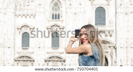 Pretty tourist teenager taking a photo with her mobile phone in Duomo square, the main landmark of Milan, Italy