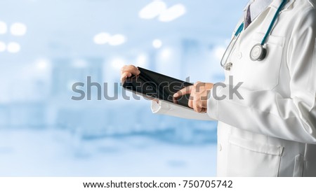 Male doctor using tablet computer to analyze patient health data record, standing on hospital background. Medical technology concept.