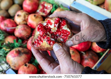 Half of the ripe pomegranate fruit in the hands of the seller in the greek vegetable shop on the background of pomegranate fruits. Horizontal. Outdoor. Close-up.