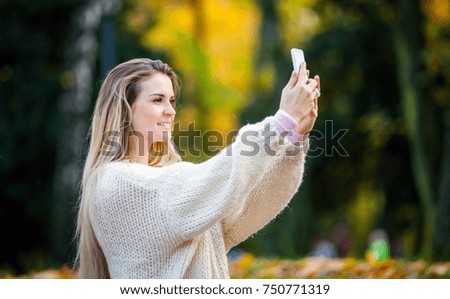 Woman in warm sweater taking picture by mobile phone walking in the autumn park