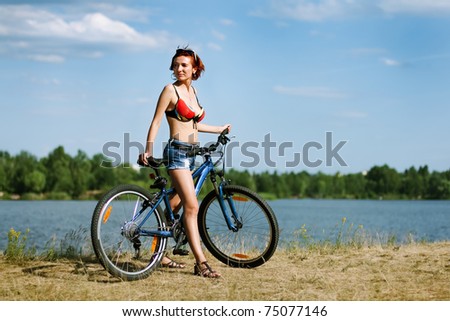 beautiful young woman on a bicycle at the background of the river and the blue sky