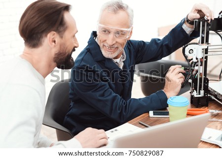 Two engineers print the details on the 3d printer. An elderly man controls the process. The second man is sitting at the laptop. They printed an apple model on the 3d printer.