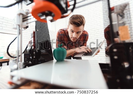 A man with a laptop in his hands controls the process of printing a 3d printer. 3d printer has printed model of an apple. The man controls the process.
