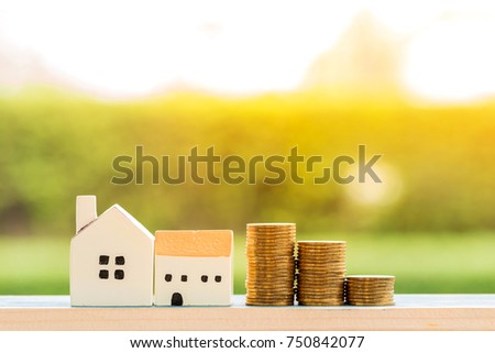 A wooden home and stacking gold coins put on the wood on sunlight in the public park, loan for a buy a new house and real estate for business investment concept.