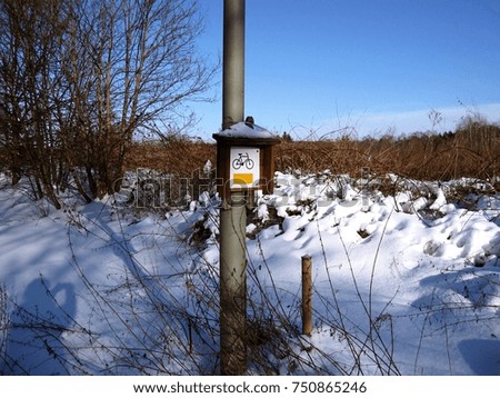 Snow-covered bicycle lane, Bike trail sign on steel pole in the forest, Winter in Poland