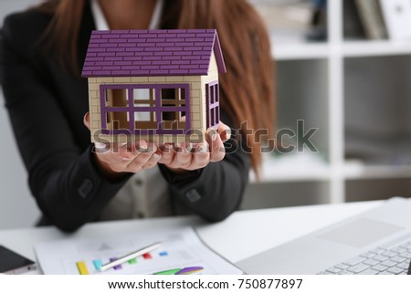 Businesswoman in the office holds a miniature toy house in her hand the subject of real estate services sales of renting the construction of apartments and housing for families.