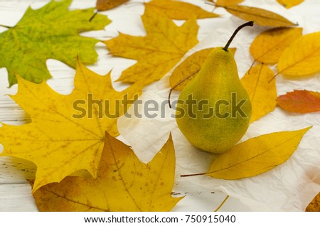 Dry colored autumn leaves around the pear on white parchment paper on vintage wooden table