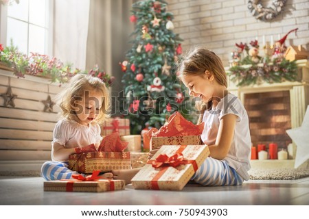 Merry Christmas and Happy Holidays! Cheerful cute childrens girls opening gifts. Kids wearing pajamas having fun near tree in the morning. Loving family with presents in room.