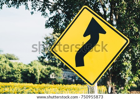Yellow color of Traffic Signs on road (curve) with colorful blurred beautiful marigold garden farm on the way in vintage filter tone.travel concept with copy space.
