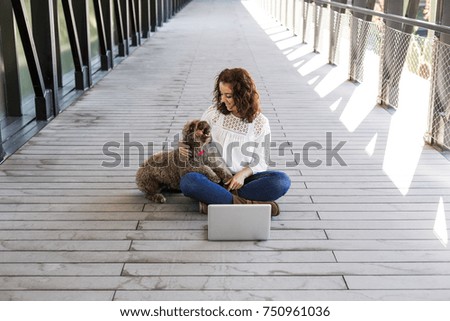 beautiful young woman having fun with her cute brown dog and working on laptop. Indoors