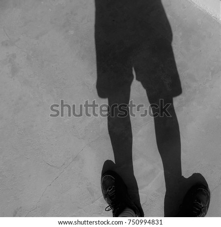 Shadow of a man standing on his shadow shoes, creating a slightly unreal image. Monochrome.