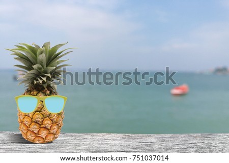 Blurred sea and ocean background with hipster fashion pineapple wearing a sunglasses and relaxing on the table board