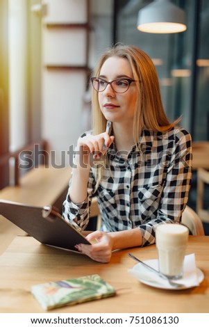 Blonde woman sitting on the chair in cafe place, working on paper work and drink coffee