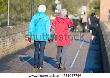 touching picture of old couple in love holding hands in waterproof coats crossing a bridge 