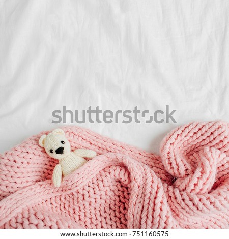 A small knitted baby toy-bear is covered with a warm blanket, flat lay,  top view Royalty-Free Stock Photo #751160575