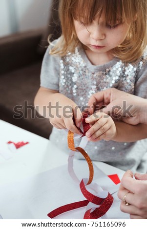 Young girl in sequin dress making a Christmas paper chain. Lifestyle image, shallow depth of field.