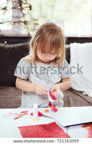 3 year old girl making a Christmas garland with red glitter paper. Lifestyle image, shallow depth of field.