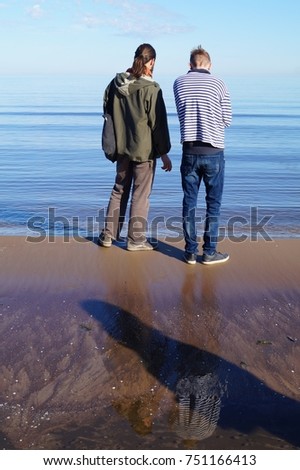 Two stay on the shore of the Baltic Sea.  Reflection in water and shadow