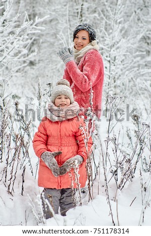 Mom with a little daughter spend a day off in the winter forest. They run through snowdrifts, they sniff snow from the frozen branches of trees and ride on sleds.