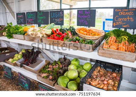 Variety of Produce in Bins in Farm Roadside Stand: organic carrots, beets, bell peppers, cabbage, leeks, celery, rainbow chard, hot peppers, onions, and cauliflower.  Produce labeled on black boards.