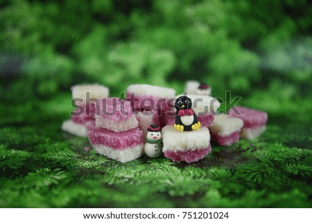 Christmas photography picture of old fashioned English coconut ice confectionery in pink and white colors with seasonal snowman decoration on contrasting green pine tree pattern background 