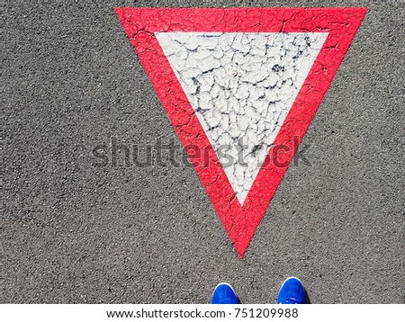 Man standing on inverted white with red border triangular road sign yield that you need to wait and give others the right to pass