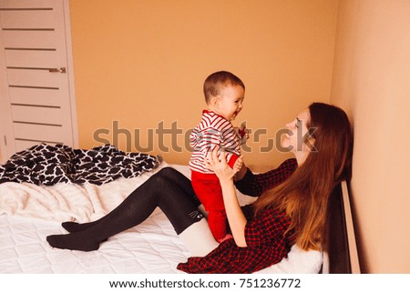 Woman with long red hair plays with little boy on bed
