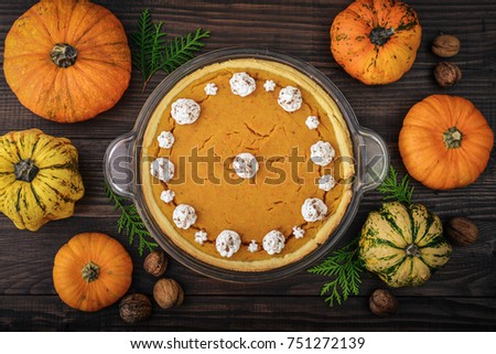 Pumpkin pie with  whipped cream and raw pumpkins on wooden background