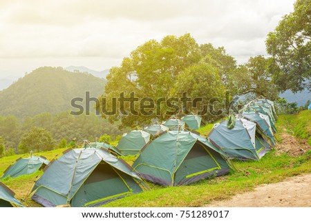 The tourist tents on meadow at the mountain with mountain view and trees with the long  distant blue mountain and white sky and white cloud.