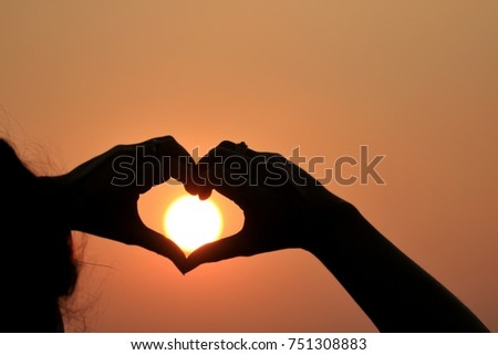  silhouette of woman hands  heart-shaped in evening, with sunset in winter.